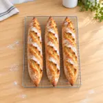Three golden, flour-dusted Easy Homemade Baguettes cooling on a wire rack