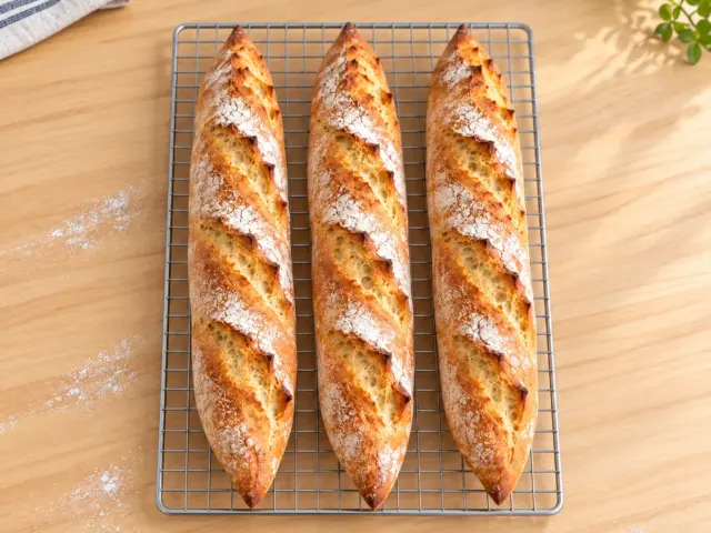 Three golden, flour-dusted Easy Homemade Baguettes cooling on a wire rack