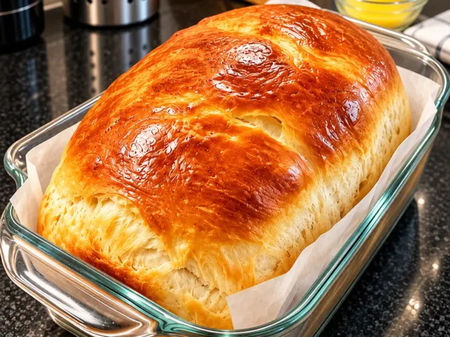 Glossy golden buttermilk sandwich bread loaf in a clear glass pan