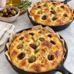 Two golden mini olive focaccias in parchment-lined skillets