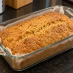 Golden red lentil loaf in a parchment-lined glass pan on a dark kitchen counter