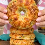 Golden cheesy zucchini cottage cheese bagel held above a stack on a wooden board
