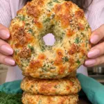 Golden cottage cheese dill bagel bread with melted cheese and sesame seeds held above a stack