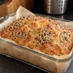 Golden cottage cheese loaf with everything seasoning and optional cheese topping in a glass pan