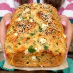 Golden cottage cheese feta herb loaf with sesame crust held over a wooden board