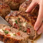 Sliced browned mini beef meat loaf showing mozzarella, tomato, bacon, and parsley on a white platter