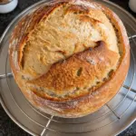 Golden round sourdough loaf with a sweeping score cooling on a circular wire rack